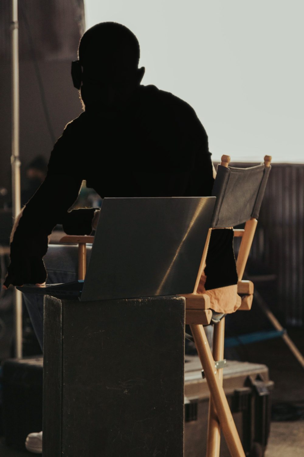 A producer on set at a laptop beside a director’s chair, backlit by the sun